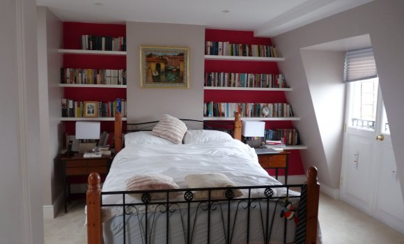 Bedroom with double bed, red wall with bookshelf