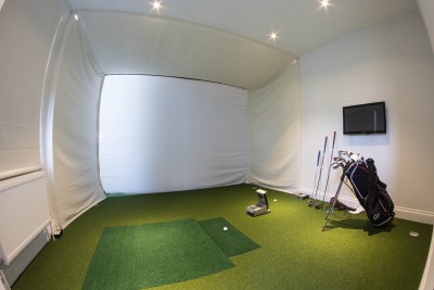 Small room to play a golf with green carpet and white walls