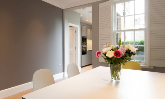 Completely refurbishment dining room with white table, chairs, grey walls and big window